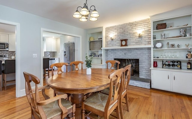 dining space featuring a fireplace, light wood-style flooring, a notable chandelier, and built in features