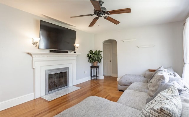 living room featuring baseboards, arched walkways, ceiling fan, and a fireplace with flush hearth