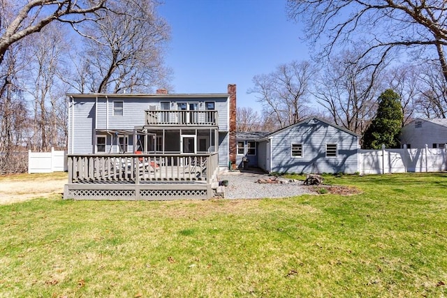 rear view of house with a balcony, a chimney, a deck, a lawn, and fence