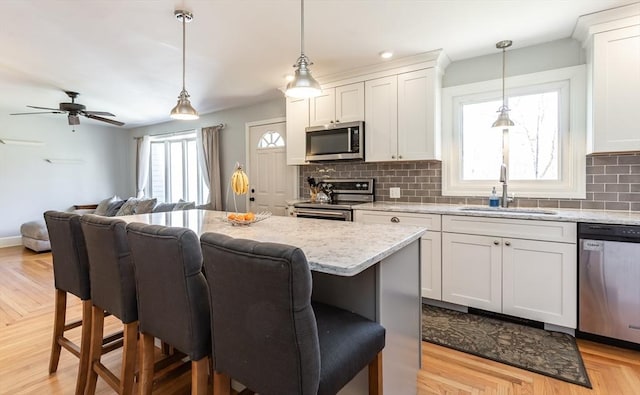 kitchen with a sink, a breakfast bar, backsplash, appliances with stainless steel finishes, and open floor plan