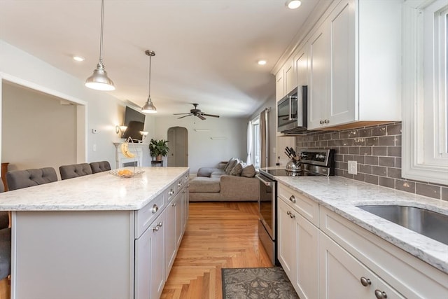 kitchen with decorative backsplash, appliances with stainless steel finishes, ceiling fan, a kitchen island, and open floor plan