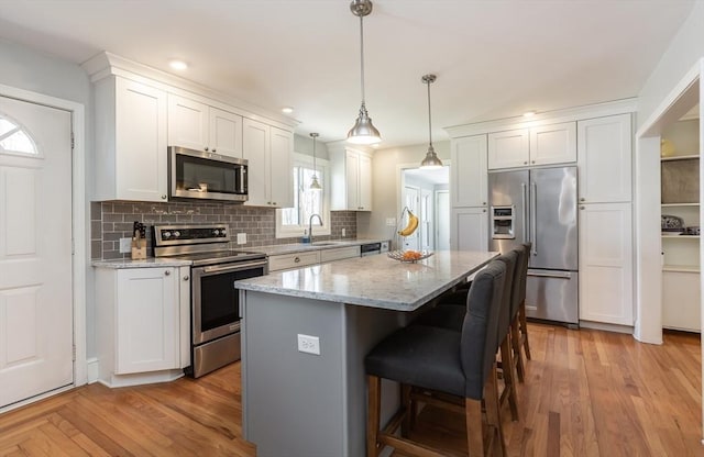 kitchen featuring decorative backsplash, appliances with stainless steel finishes, a kitchen island, white cabinets, and a sink