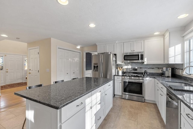 kitchen with sink, dark stone countertops, stainless steel appliances, a center island, and white cabinets