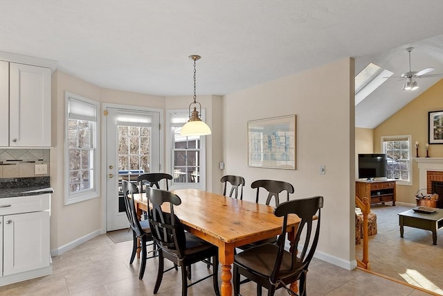 dining room featuring ceiling fan, vaulted ceiling, a brick fireplace, and light tile patterned floors