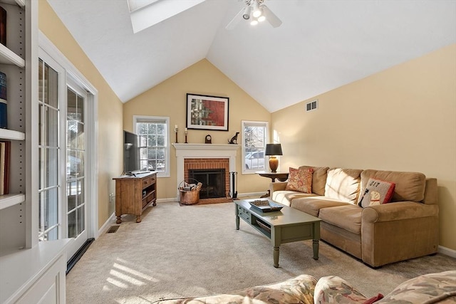 carpeted living room with a brick fireplace, lofted ceiling with skylight, and ceiling fan