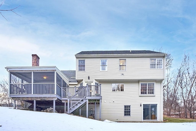 snow covered house with a wooden deck and a sunroom