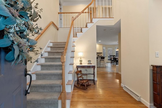 staircase featuring hardwood / wood-style flooring, ornamental molding, baseboard heating, and a high ceiling