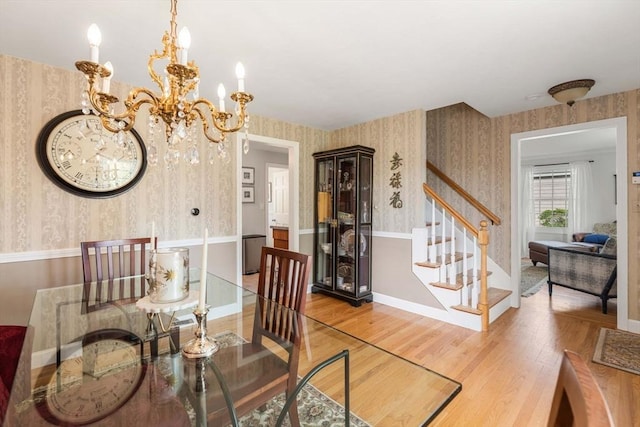 dining area with stairway, an inviting chandelier, wallpapered walls, and wood finished floors