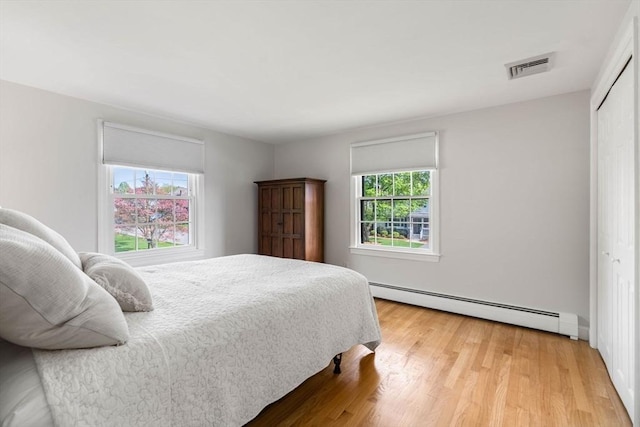 bedroom with a baseboard radiator, light wood finished floors, visible vents, and a closet