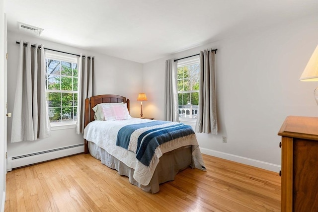 bedroom featuring a baseboard radiator, light wood-style flooring, visible vents, and multiple windows