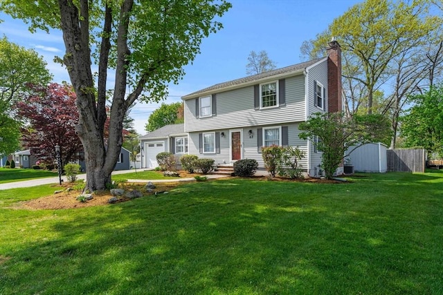 colonial house with fence, an attached garage, a front yard, a chimney, and central AC unit