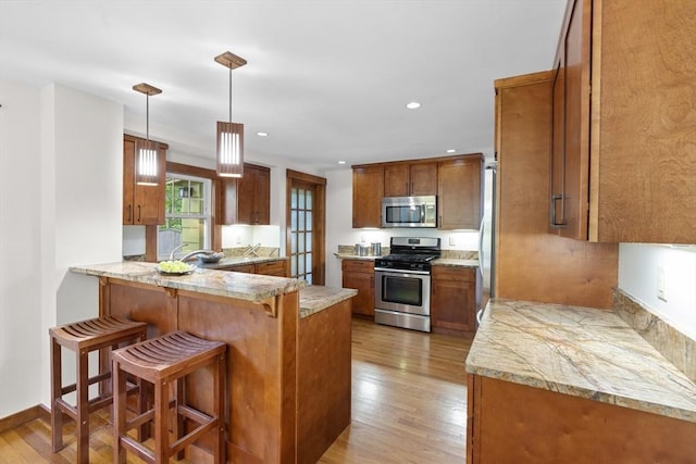 50 Grove Hill Park, Newton, MA 02460 - kitchen with light wood finished floors, a kitchen breakfast bar, brown cabinetry, stainless steel appliances, and a peninsula