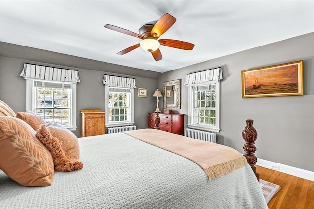 bedroom with radiator heating unit, baseboards, ceiling fan, and wood finished floors