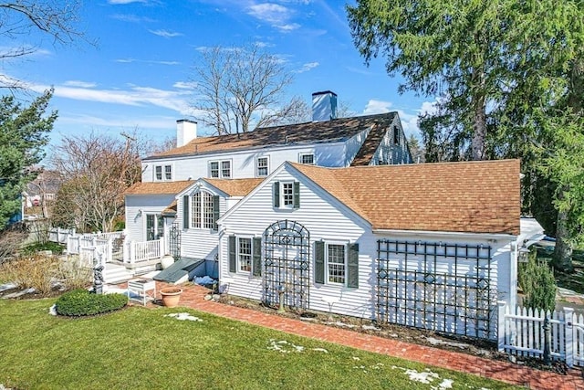 back of property with a chimney, fence, a lawn, and roof with shingles