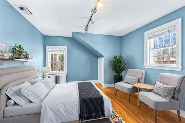 bedroom with multiple windows, radiator heating unit, wood finished floors, and visible vents