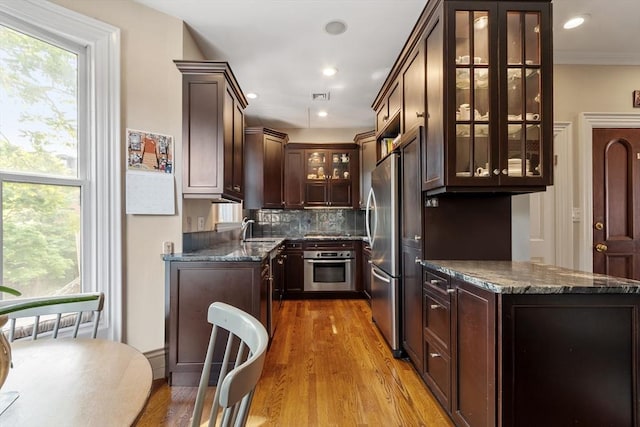 38 Concord Sq Unit 2, Boston, MA 02118 - kitchen featuring appliances with stainless steel finishes, dark brown cabinets, tasteful backsplash, light wood-type flooring, and glass insert cabinets