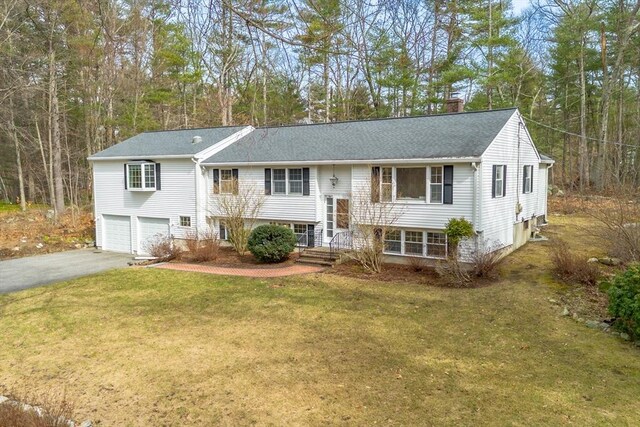 split foyer home with aphalt driveway, a shingled roof, a front yard, an attached garage, and a chimney