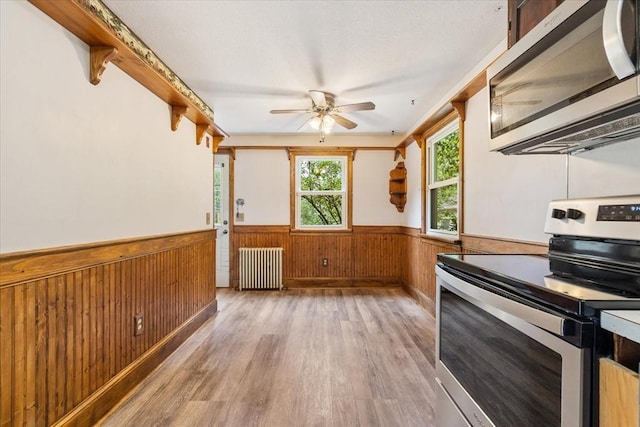 61 Mattawa Cir, Orange, MA 01364 - kitchen with appliances with stainless steel finishes, radiator, a wainscoted wall, light wood-type flooring, and a ceiling fan