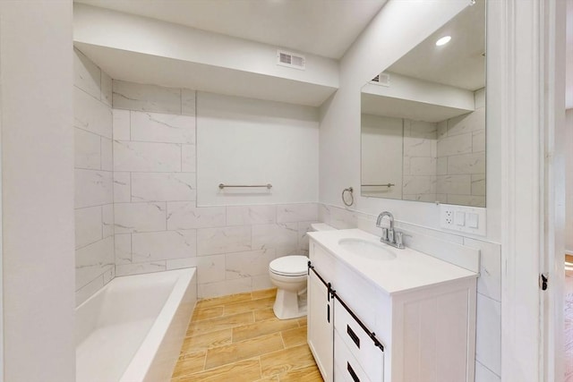 full bathroom featuring visible vents, tile walls, toilet, a tub to relax in, and vanity