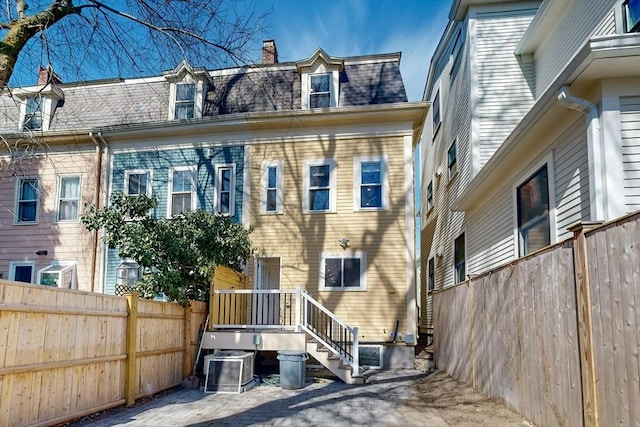 back of house featuring mansard roof, a shingled roof, central AC, and fence