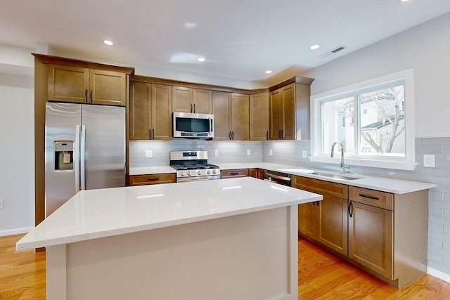 kitchen featuring light stone counters, light wood-style flooring, a sink, appliances with stainless steel finishes, and a center island