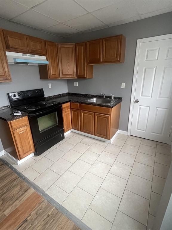422 County St, Fall River, MA 02723 - kitchen featuring black / electric stove, under cabinet range hood, a drop ceiling, a sink, and brown cabinets