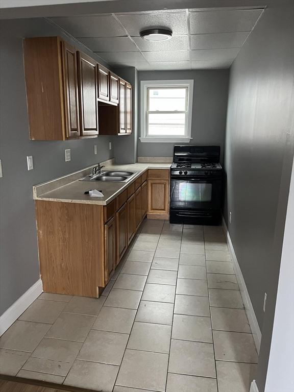 422 County St, Fall River, MA 02723 - kitchen with black gas range, a sink, baseboards, light countertops, and light tile patterned floors