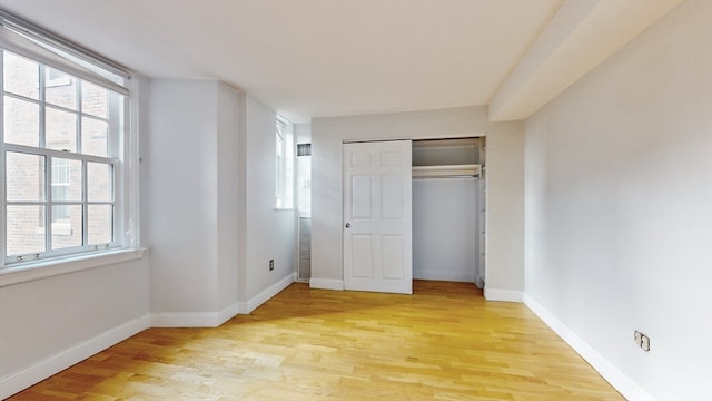 unfurnished bedroom with light hardwood / wood-style floors, multiple windows, and a closet