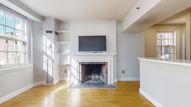 unfurnished living room with a brick fireplace, light hardwood / wood-style floors, a healthy amount of sunlight, and built in shelves