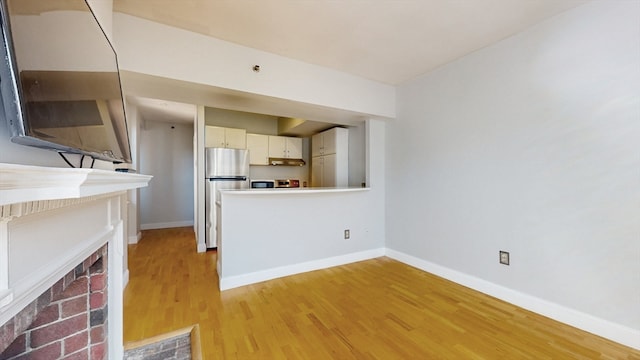 kitchen with stainless steel refrigerator, white cabinetry, and light hardwood / wood-style flooring