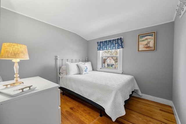 bedroom with wood finished floors, vaulted ceiling, baseboards, and ornamental molding