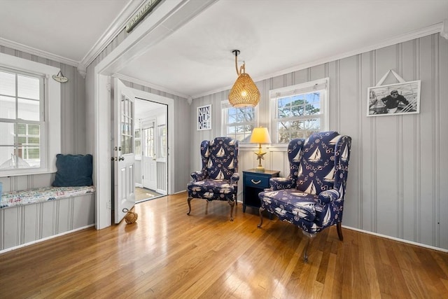 sitting room with wood-type flooring, healthy amount of natural light, crown molding, and a decorative wall