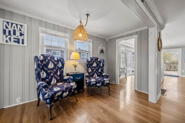 living area with crown molding, wood finished floors, a decorative wall, and baseboards