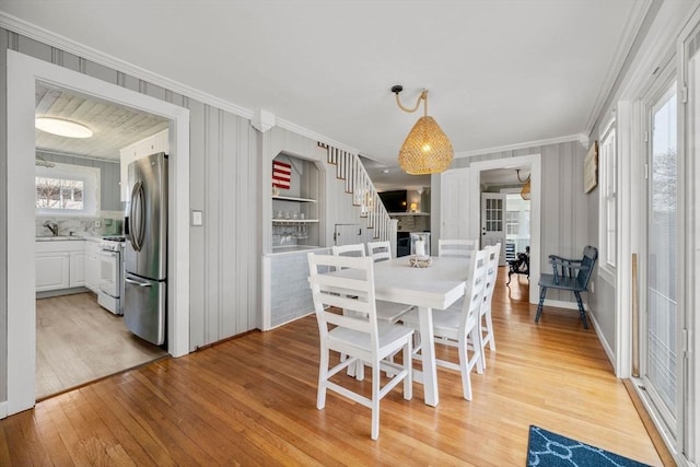 dining space featuring ornamental molding, light wood-type flooring, stairs, and healthy amount of natural light