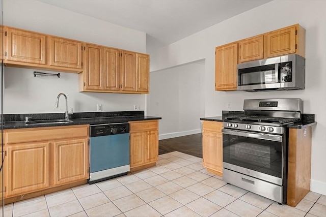 kitchen featuring sink, light tile patterned flooring, dark stone counters, and appliances with stainless steel finishes