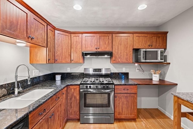 kitchen featuring under cabinet range hood, light wood-style flooring, appliances with stainless steel finishes, brown cabinets, and a sink