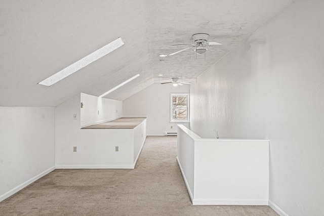 bonus room featuring lofted ceiling with skylight, light carpet, a ceiling fan, a textured ceiling, and baseboards