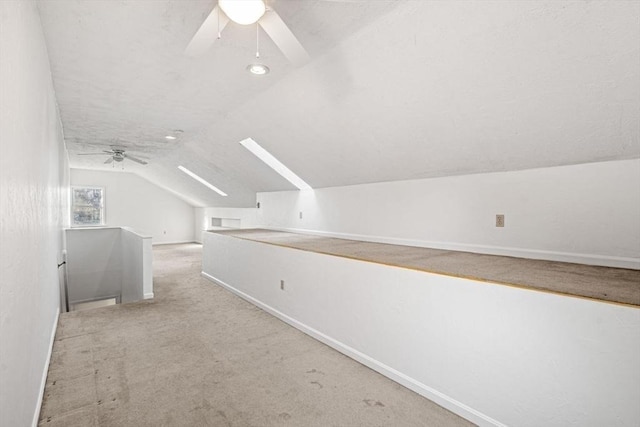 bonus room with lofted ceiling with skylight, ceiling fan, baseboards, and carpet