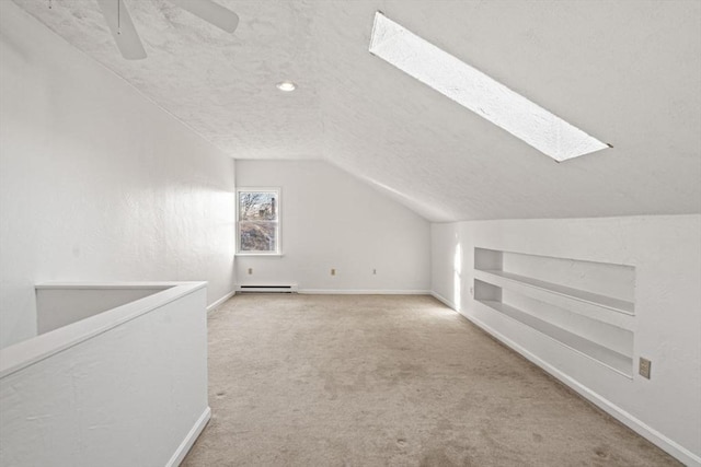 additional living space featuring built in shelves, a textured ceiling, vaulted ceiling with skylight, carpet, and baseboard heating