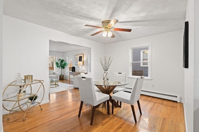 dining space with baseboards, light wood finished floors, ceiling fan, a textured ceiling, and a baseboard heating unit