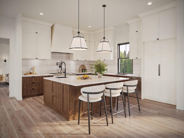 kitchen with pendant lighting, decorative backsplash, a center island with sink, and white cabinets