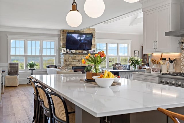 27 Gully Ln, Sandwich, MA 02537 - kitchen with wall chimney exhaust hood, a fireplace, light wood-style floors, white cabinetry, and light stone counters