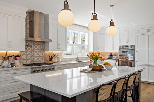 27 Gully Ln, Sandwich, MA 02537 - kitchen featuring wall chimney exhaust hood, appliances with stainless steel finishes, a breakfast bar area, a kitchen island, and white cabinetry