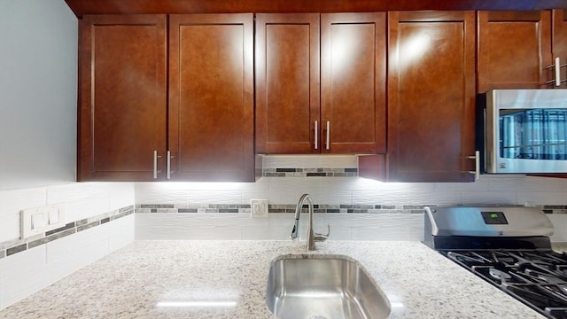 kitchen with backsplash, light stone countertops, sink, and gas range oven