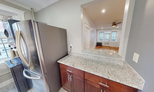 kitchen featuring stainless steel refrigerator, ceiling fan, light stone counters, and ornamental molding