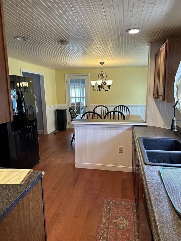 10 Marilyn Dr, Auburn, MA 01501 - kitchen featuring black fridge, dark countertops, a wainscoted wall, a chandelier, and dark wood-style flooring