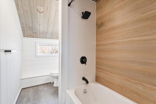 bathroom featuring wooden walls, toilet, and tiled shower / bath