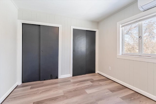 unfurnished bedroom with light wood-type flooring and a wall unit AC