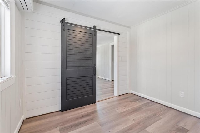 spare room featuring an AC wall unit, ornamental molding, light hardwood / wood-style floors, and a barn door