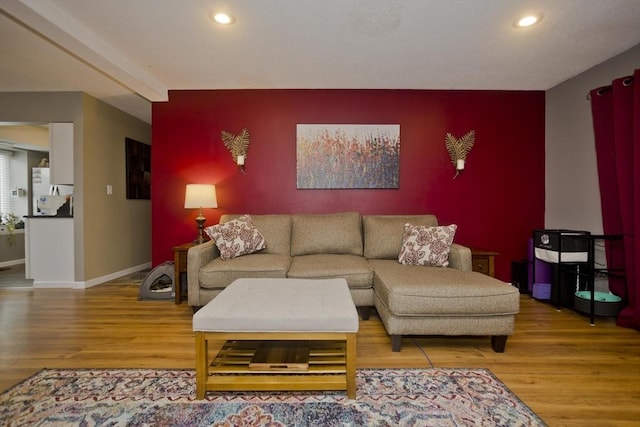 living room featuring an accent wall, baseboards, wood finished floors, and recessed lighting